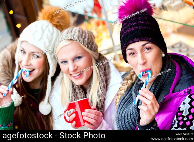 Women drinking mulled wine in mugs and eating candy sticks on German Christmas Market
