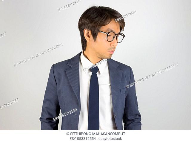 Young Asian Portrait Businessman in Navy Blue Suit Wear Eyeglasses and Look Below on Grey Background
