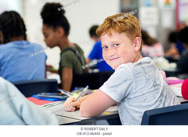Portrait smiling, confident junior high school boy student studying at desk in classroom