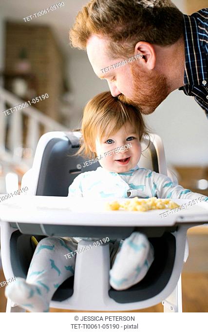 Father kissing head of his baby girl in high chair