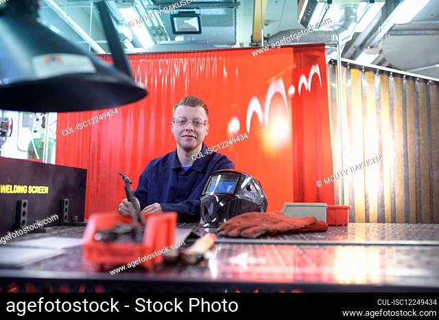 A male student sitting at a welding bench beside a welding mask
