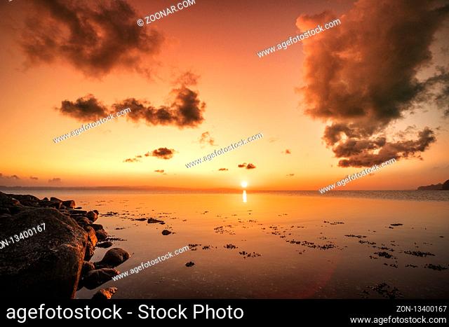 Sunrise over the sea by the shore with rocks in the morning sun