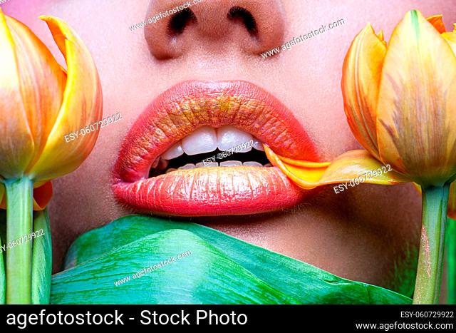 closeup of beautiful young woman with orange lips and yellow tulip flowers touching them
