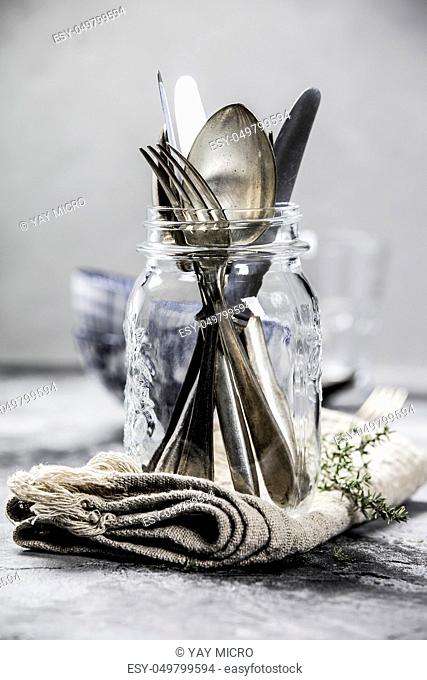 Forks spoons and knifes in a glass jar on grey vintage background