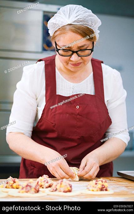 Adult woman in glasses and apron bakes cakes in the bakery full face close-up