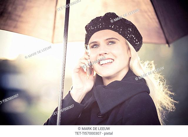 Smiling woman under umbrella using mobile phone