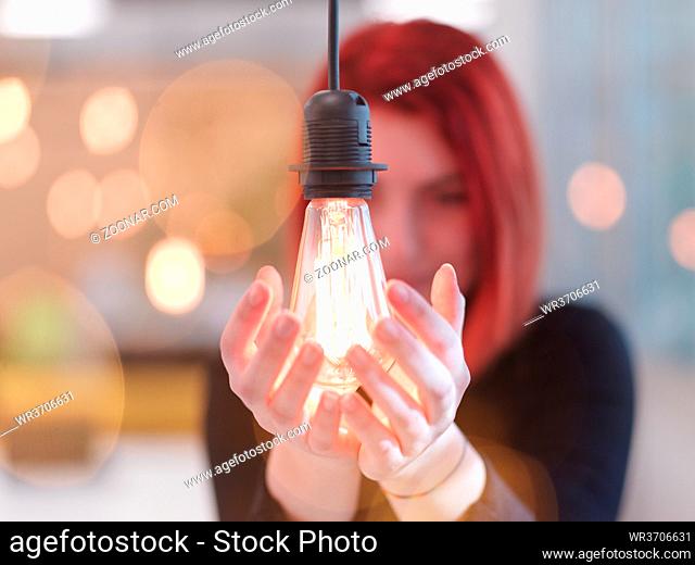 redhead businesswoman at office holding a hand around light bulb representing concept of business solutions idea and green energy