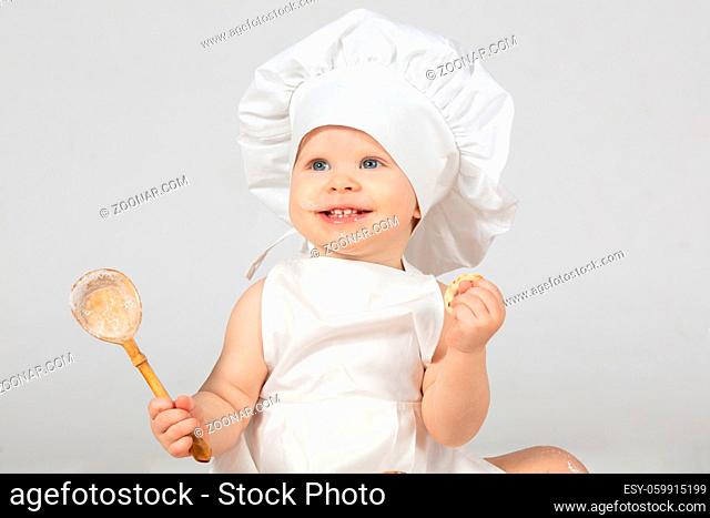 Child cook. Beautiful little girl in cook clothes with a big spoon. The child is one year old. Funny baby is laughing. Little chef