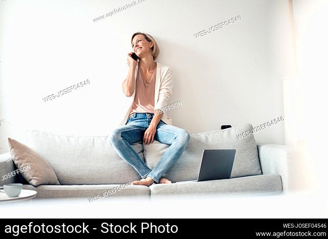 Happy woman talking on mobile phone while sitting in front of wall at home