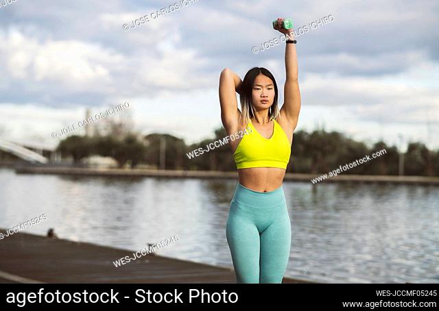 Dedicated woman practicing exercise with dumbbell on jetty