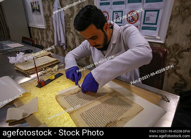 22 March 2021, Iraq, Najaf: Restorer Mostafa Majed works on a religious manuscript, believed to be written by Imam Ali ibn Abi Talib