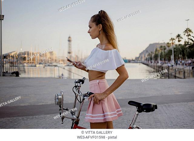 Fashionable young woman exploring Barcelona with a bicycle, using smartphone