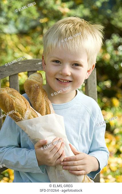 Blond boy holding two baguette sticks in paper