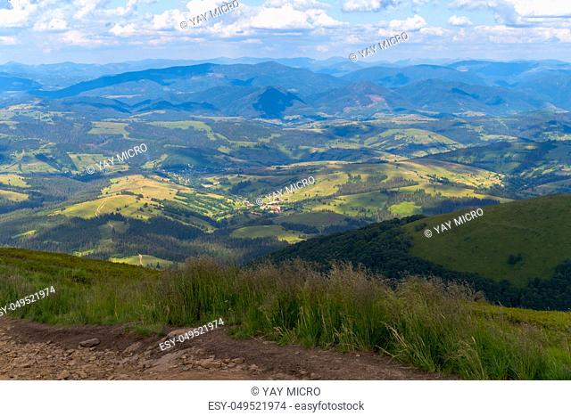 A magnificent landscape from the top of the mountain to other mountains and hills is covered with forest plantations and green grass over which the white clouds...