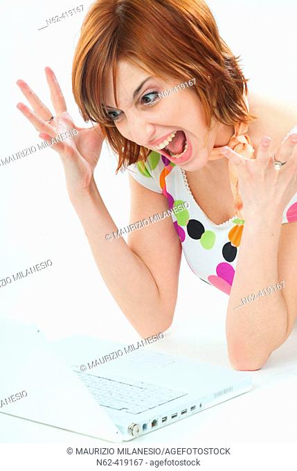 Girl with red hair screaming angry with  mouth open and hands raised in front of her laptop