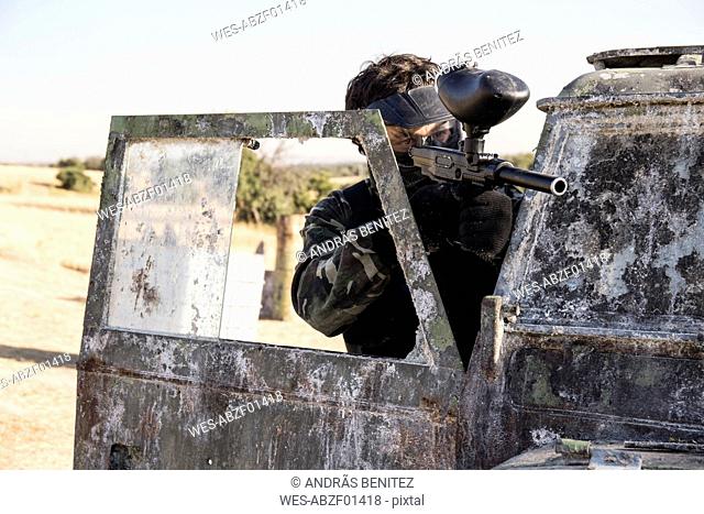 Paintball player aiming with paintball gun behind the door of an abandonated car