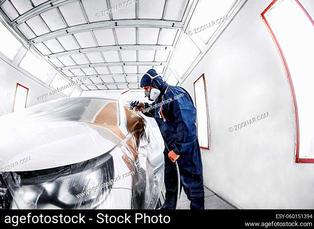worker painting a white car in a special garage, wearing a costume and protective gear