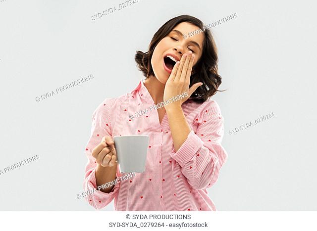 happy yawning young woman in pajama with coffee