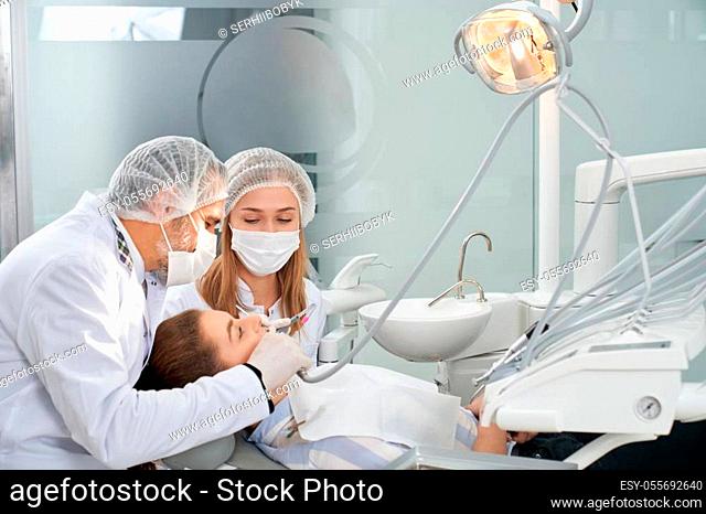Modern stomatology private clinic with professional equipment. Dentists working with client's teeth. Woman lying on dentist cahir