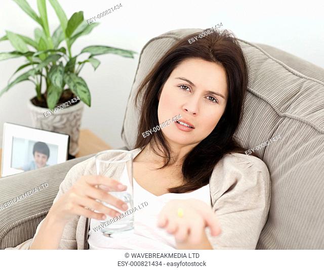 Tired woman taking her medicine lying on the sofa at home