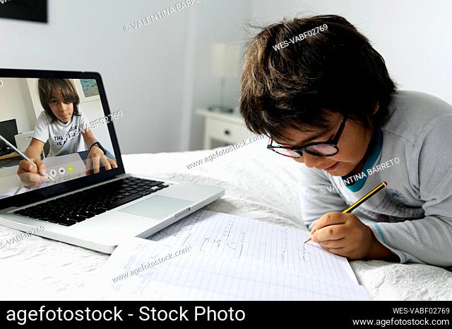 Little boy lying on bed using laptop for video chat