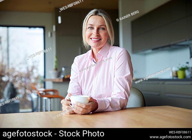 Smiling blond woman holding coffee cup sitting at table