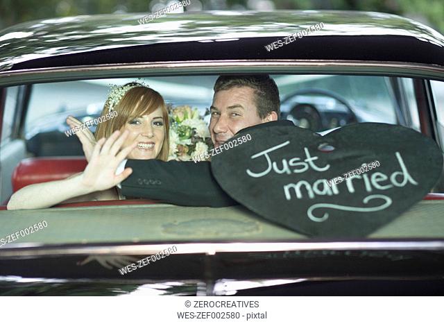 Happy bride and groom waving in car after the wedding