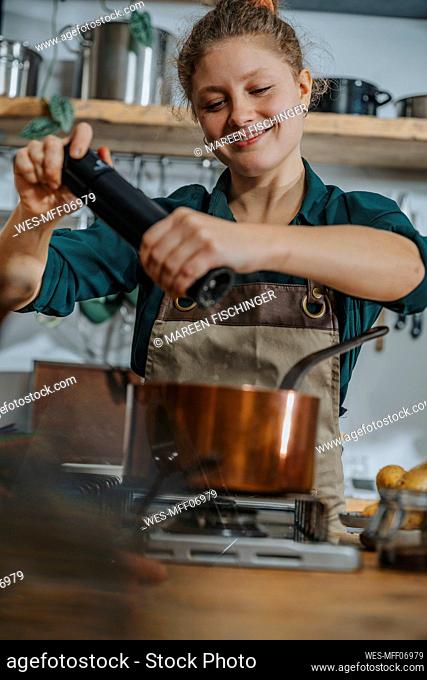 Smiling chef adding pepper in food while cooking in kitchen