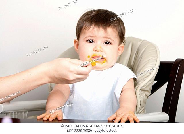 Cute baby infant boy girl expresses dislike disgust for food fed by spoon