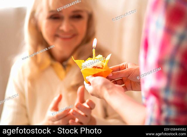 Close Shot Of Tasty Cupcake In Orange Wrapper Being Gives To Senior Mother While The Birthday Candle Are Burning