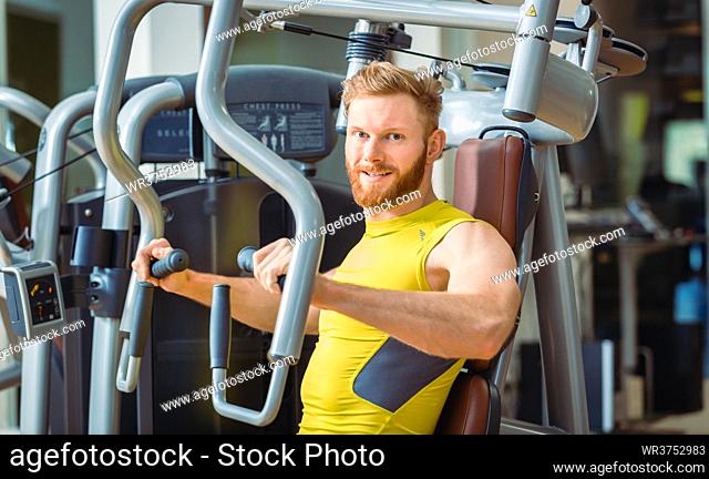 Portrait of a handsome bodybuilder smiling and looking at camera while exercising at a modern fitness machine for pectoral fly and deltoid workout