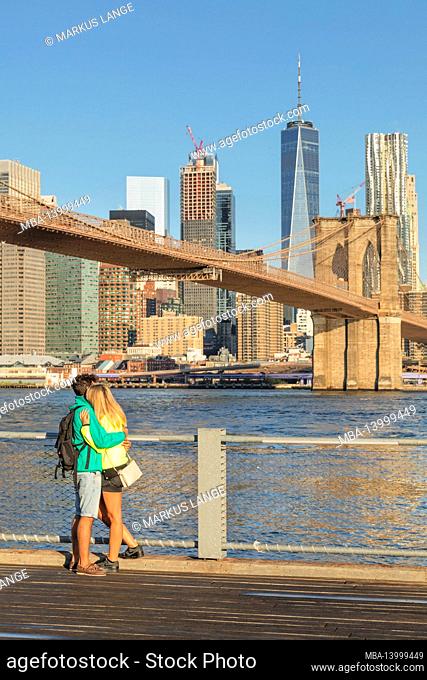couple in front of manhattan skyline with brooklyn bridge and one world trade center, new york city, usa