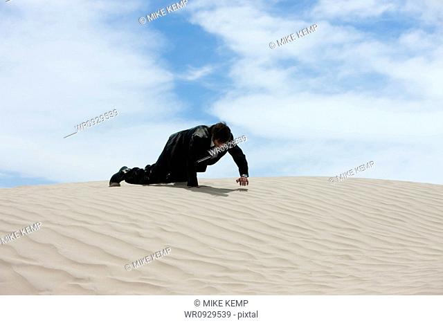 USA, Utah, Little Sahara, mid adult businessman crawling over sand dune