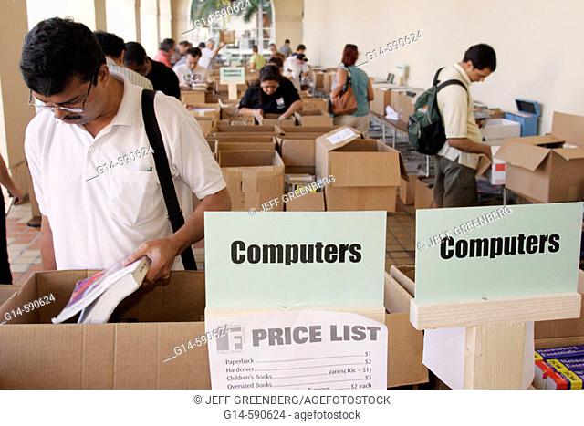 Book sale, boxes, browsing, sign, computers, price list, Asian man.  Miami-Dade Public Library. Miami. Florida. USA