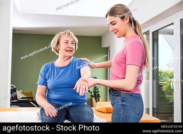 Young physiotherapist helping patient to stretch hand at home