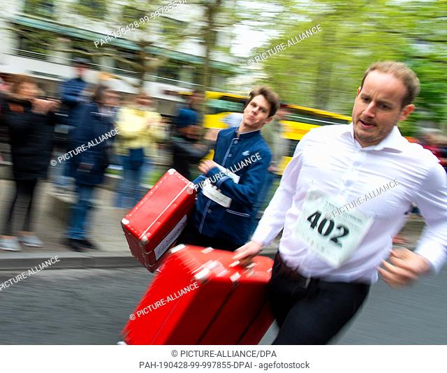 28 April 2019, Berlin: Two bellboys with filled suitcases pass the spectators at the 9th Berlin Waiter Run. Waiters, barkeepers