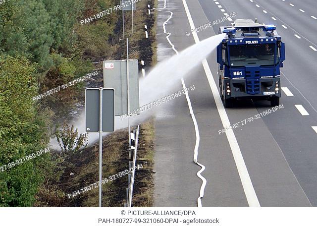 27 July 2018, Germany, Potsdam/Fichtenwalde: A police water cannon extinguishes on the edge of a forest area on the motorway
