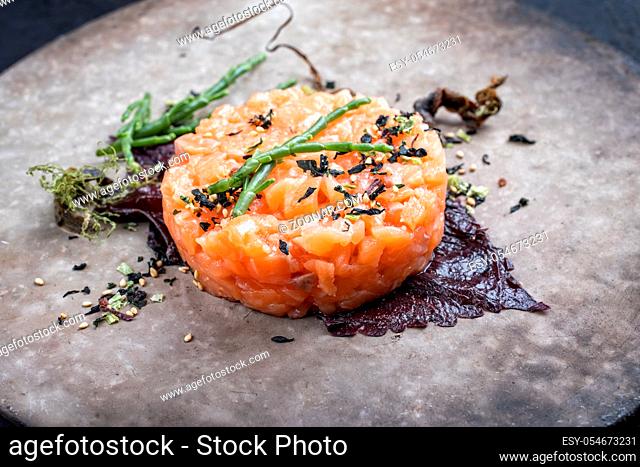Gourmet fish tartar raw from salmon fillet with glasswort, nori and Japanese spice as closeup on modern design plate