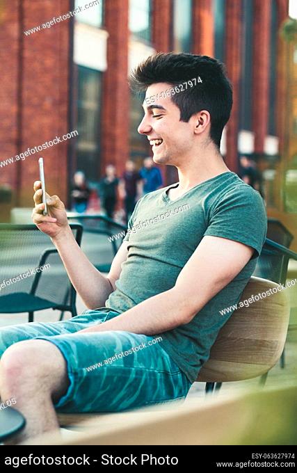 Young man having fun with smartphone, reading funny texts, sitting in center of town