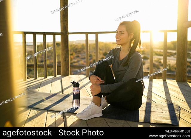 Smiling young woman contemplating while sitting on mat in gazebo during sunset