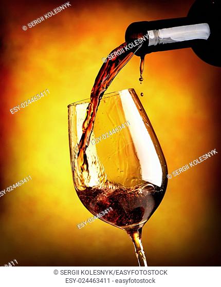 Red wine pouring in a wineglass on orange background