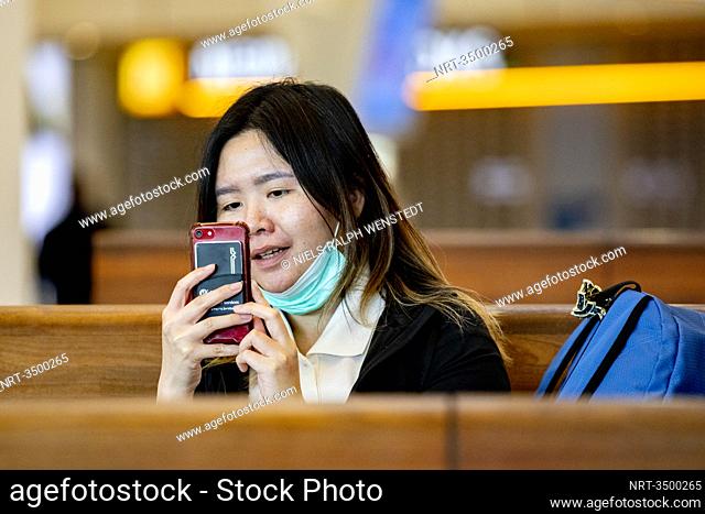 SCHIPHOL - A asian woman with mouthcap wiaiting for her next flight. Closed gates and departure halls at Schiphol during times of the corona virus