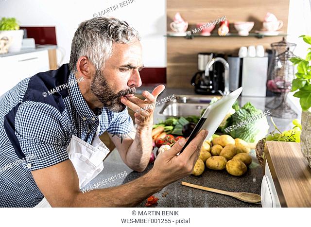 Austria, Man in kitchen holding digital tablet, looking for recipe