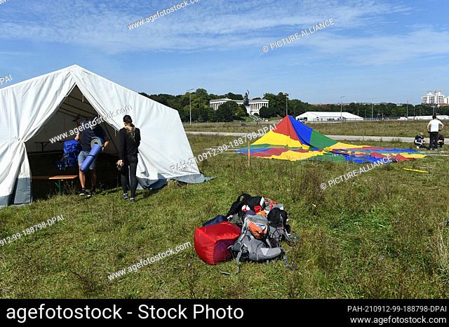 07 September 2021, Bavaria, Munich: Jona (l-r) and Marie carry luggage out of a tent under a blue sky and sunshine in the area of the protest camp on the...