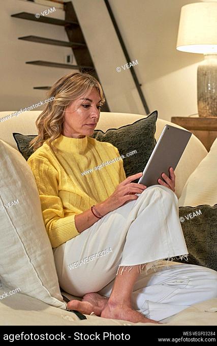 Mature woman using digital tablet while siting on lounge chair at home