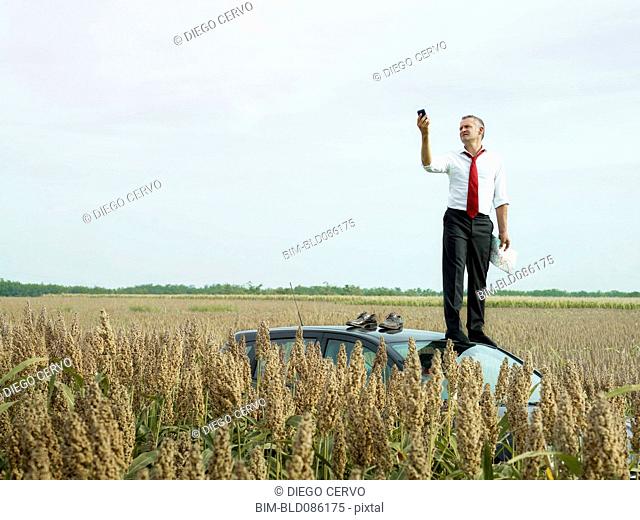 Caucasian businessman on top of car in field looking at gps device