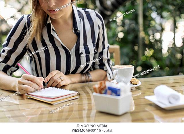 Businesswoman sitting at sidewalk cafe writing in notebook