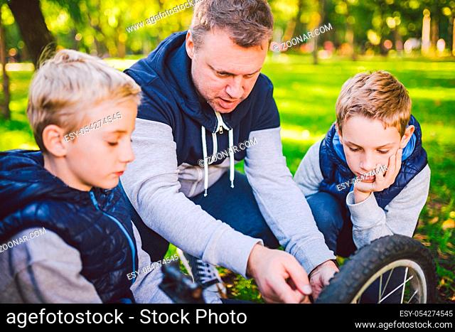 Father day. A large friendly family father and sons together actively relax in the fresh air. Dad teaches sons to repair bicycles