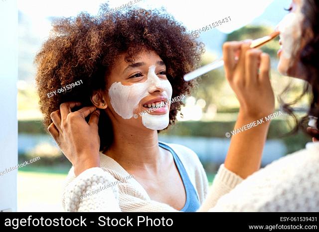 Smiling biracial female friends applying beauty cream on each others faces in balcony