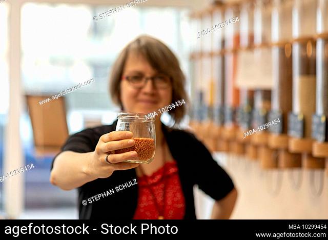 A woman holds a glass with lentils in her hand, detail from an unwrapped shop